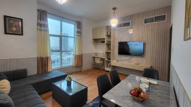 Een moderne woonkamer met een bank, een salontafel, een eettafel met stoelen, een aan de muur bevestigde televisie en een groot raam met gordijnen.