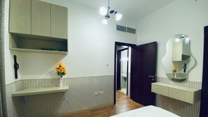 Een slaapkamer met een bed, een houten garderobe, een nachtkastje met een bloemenvaas, een spiegel en een deur naar een andere kamer.