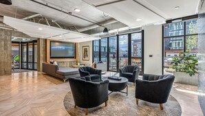 Ein moderner Lounge-Bereich mit großem Bildschirm, bequemen Sitzgelegenheiten und großen Fenstern mit Blick auf die Stadt.