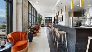 En modern hotellobby med en lång bardisk, orange sittmöbler och stora fönster med utsikt över staden.