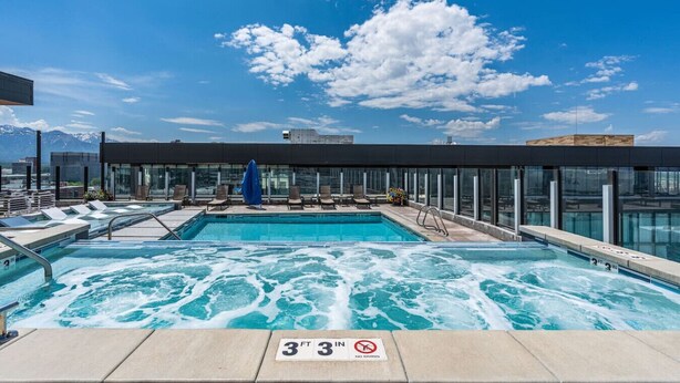 En pool på taket med ett bubbelbad, solstolar och en inglasad terrass med utsikt över bergen.