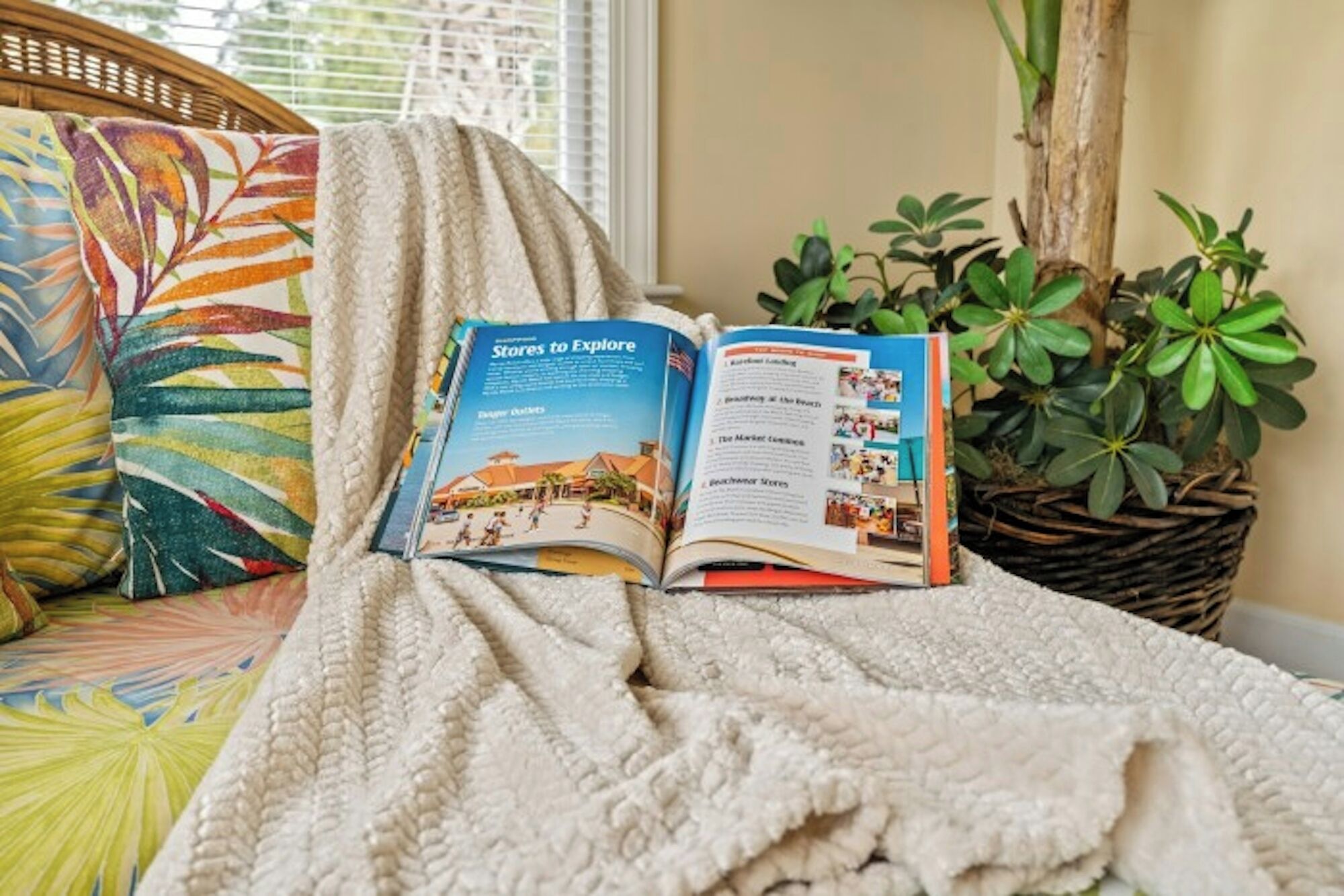 Ein Buch mit dem Titel 'Stores to Explore' auf einem Bett mit bunten Kissen und einer Topfpflanze.