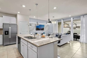 A modern kitchen with granite countertops, stainless steel appliances, pendant lighting, and a dining area with a sofa and table. - 5BD Windsor Island Resort Disney Themed (WI 3858) (Davenport)