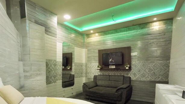 Une chambre à coucher moderne avec un grand lit, un canapé foncé, un téléviseur fixé au mur et un miroir.