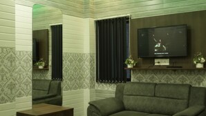 Un salon avec un plafond éclairé de lumière verte, un téléviseur à écran plat fixé au mur, un canapé et un petit meuble en bois.