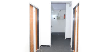 Un couloir étroit, avec deux portes de chaque côté, un extincteur fixé au mur et un luminaire au plafond.