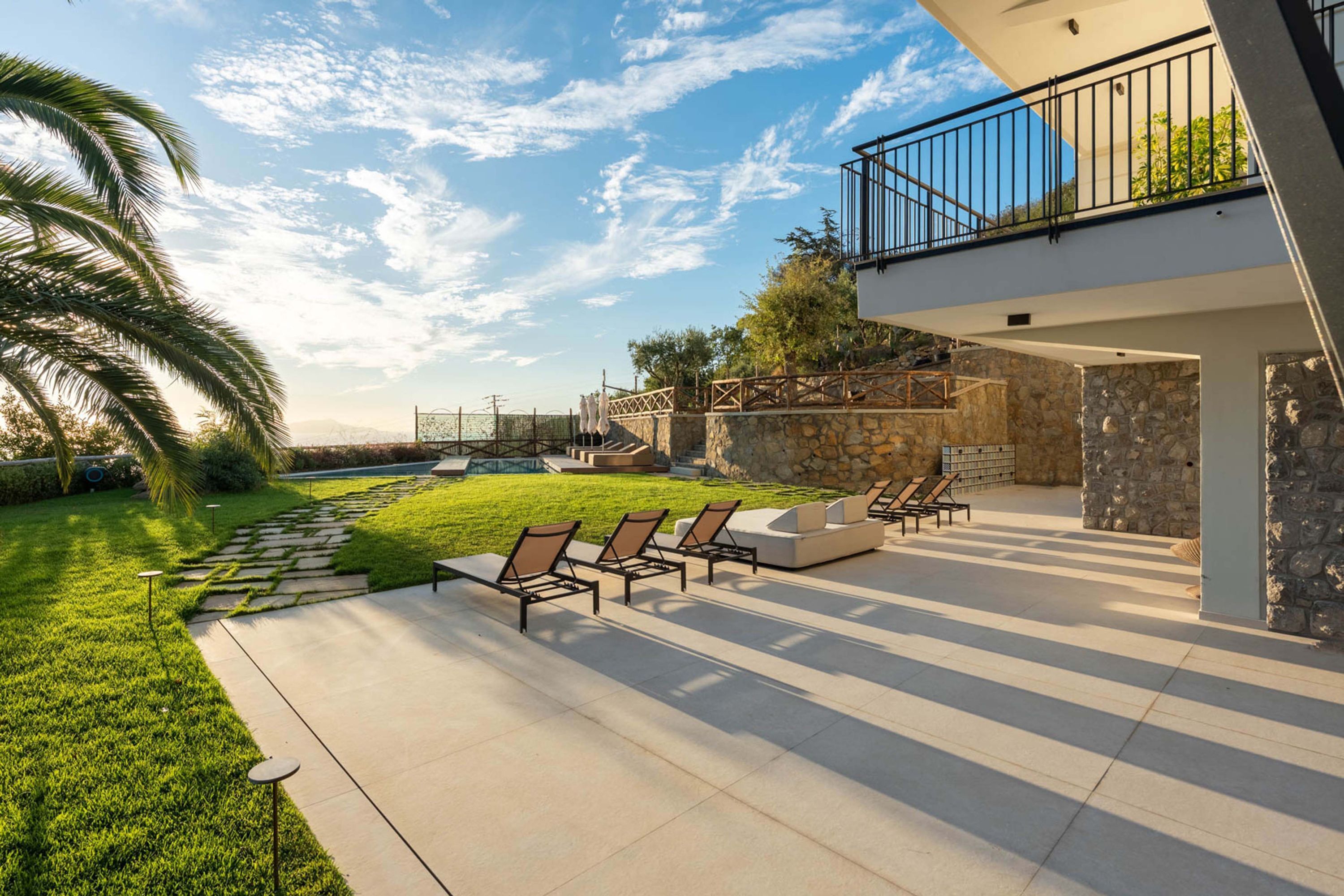 Una terrazza esterna moderna con poltrone relax, un muro in pietra e cielo sereno.