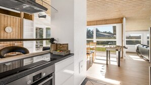 Une cuisine moderne dotée d’un four encastré, un coin repas avec une table et des chaises, et une vue sur l’extérieur grâce à de grandes fenêtres.