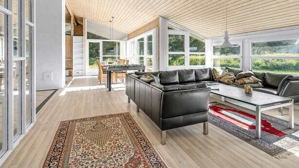 Un salon spacieux avec un plafond en bois, un canapé en cuir noir, une table basse en verre et un tapis à motifs.