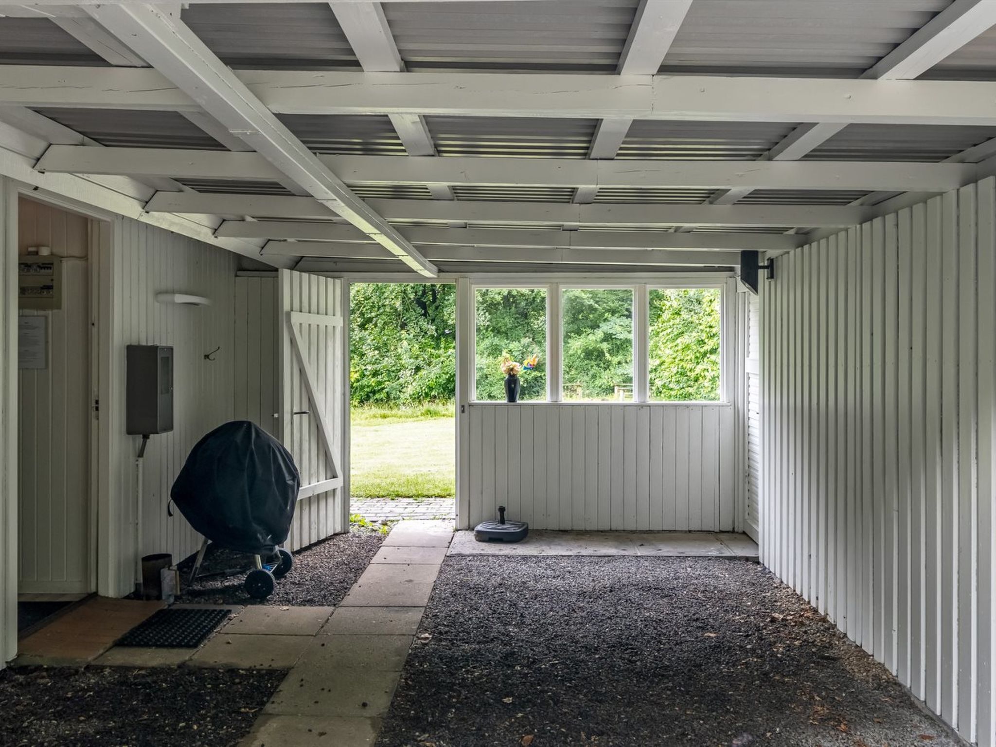 A covered garage with a gravel floor, a covered entrance, and a window overlooking a green landscape.