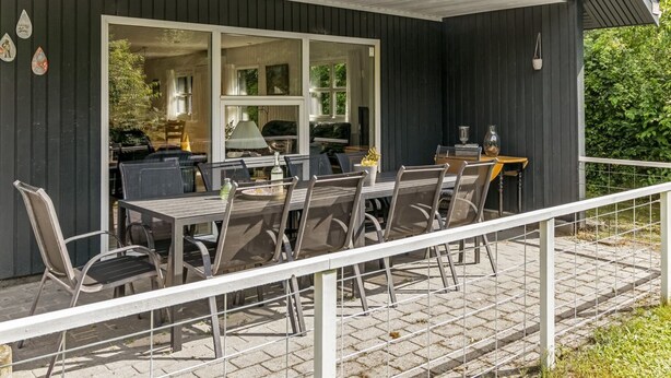 An outdoor dining area with a table and chairs, a railing, and a view of the interior through a glass door. - "Matias" - 30km from the sea by Interhome (Toftlund)
