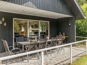 Un espace extérieur aménagé pour les repas, avec une table et des chaises, une rambarde et une vue sur l’intérieur à travers une porte vitrée.