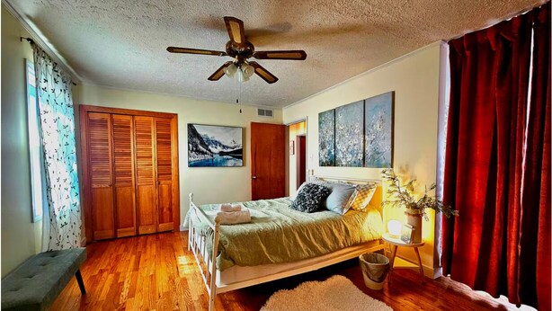 A bedroom with a wooden floor, a bed with a green bedspread, a ceiling fan, a window with curtains, and a red curtain. - Ami's Oak House - ORNL - Melton Lake - Windrock (Oak Ridge)