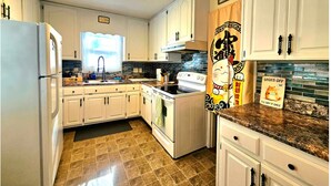 A kitchen with white cabinets, a stove, a sink, and a window. - Ami's Oak House - ORNL - Melton Lake - Windrock (Oak Ridge)