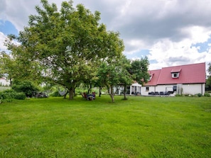 Una casa con tetto rosso, un grande albero nel giardino e un prato verde.