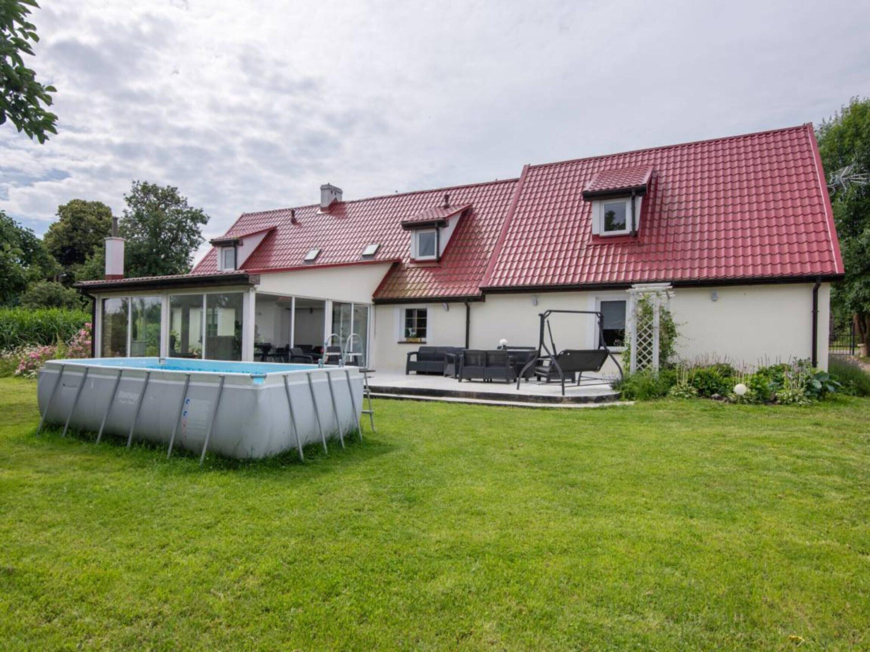 A house with a red-tiled roof, a swimming pool, and a patio area with outdoor furniture.