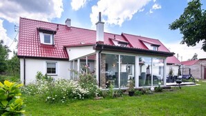 A house with a red-tiled roof, a glass conservatory, and a garden with white flowers. - Comfortable House With a Swimming Pool and Sauna (gmina Dobra)