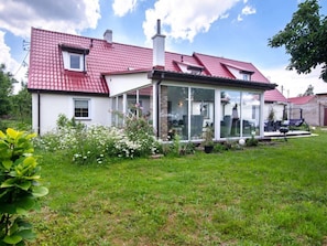 A house with a red-tiled roof, a glass conservatory, and a garden with white flowers. - Comfortable House With a Swimming Pool and Sauna (gmina Dobra)