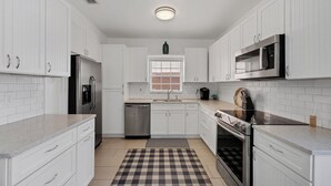 A modern kitchen with white cabinets, stainless steel appliances, a checkered rug, and a window with blinds.