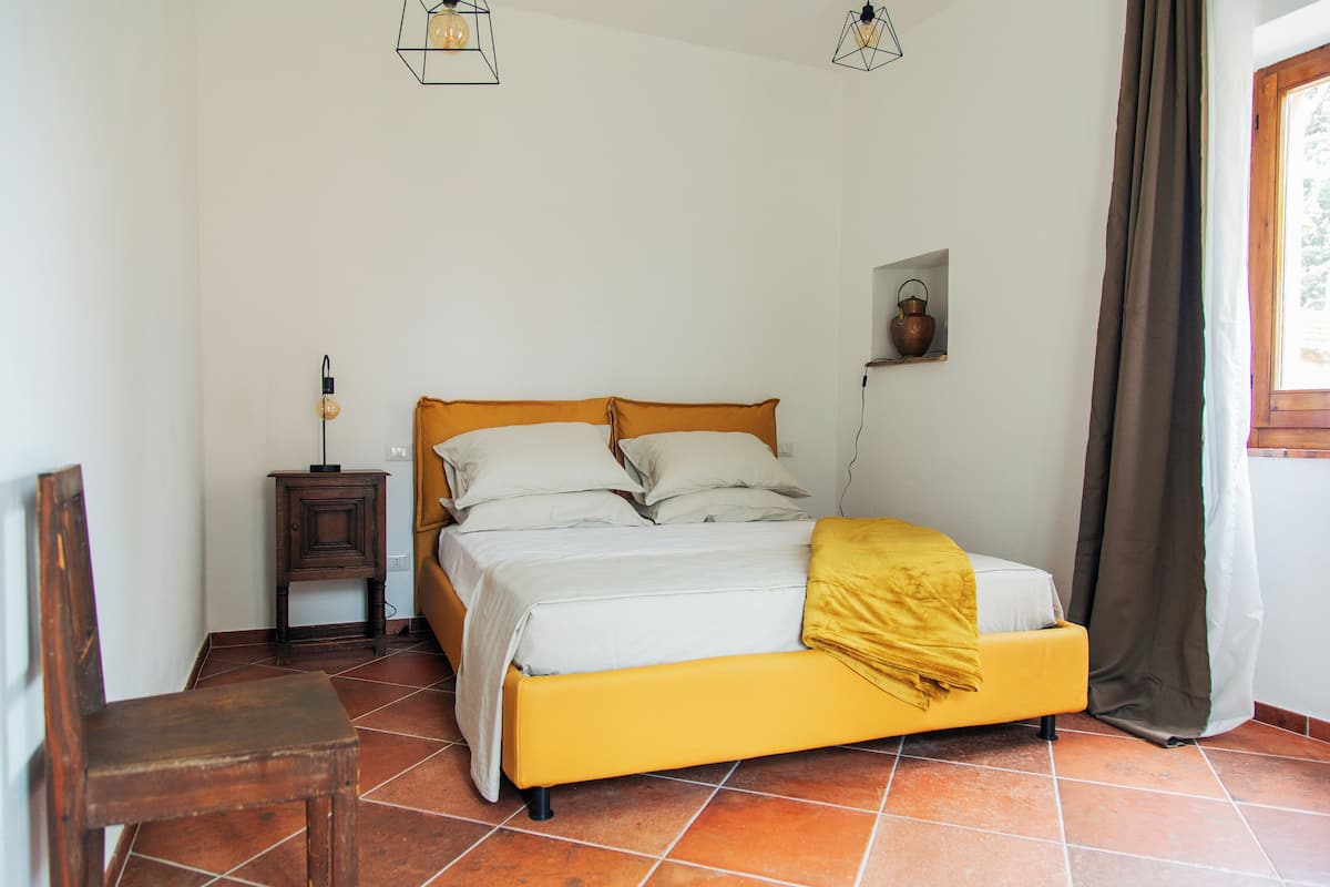 A bedroom with a bed, a bedside table, a chair, and a window with curtains.