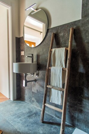 A bathroom with a modern sink, a wooden ladder, and a mirror on the wall.