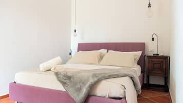 Una cama con cabecera, una mesita de noche y una lámpara fijada a la pared.