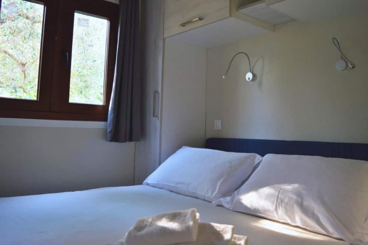 A hotel room with a bed, a window with curtains, and a wall-mounted nightlight.