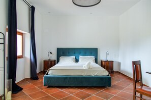 A bedroom with a large bed, two bedside tables, a chair, a window with curtains, and a ceiling light fixture.