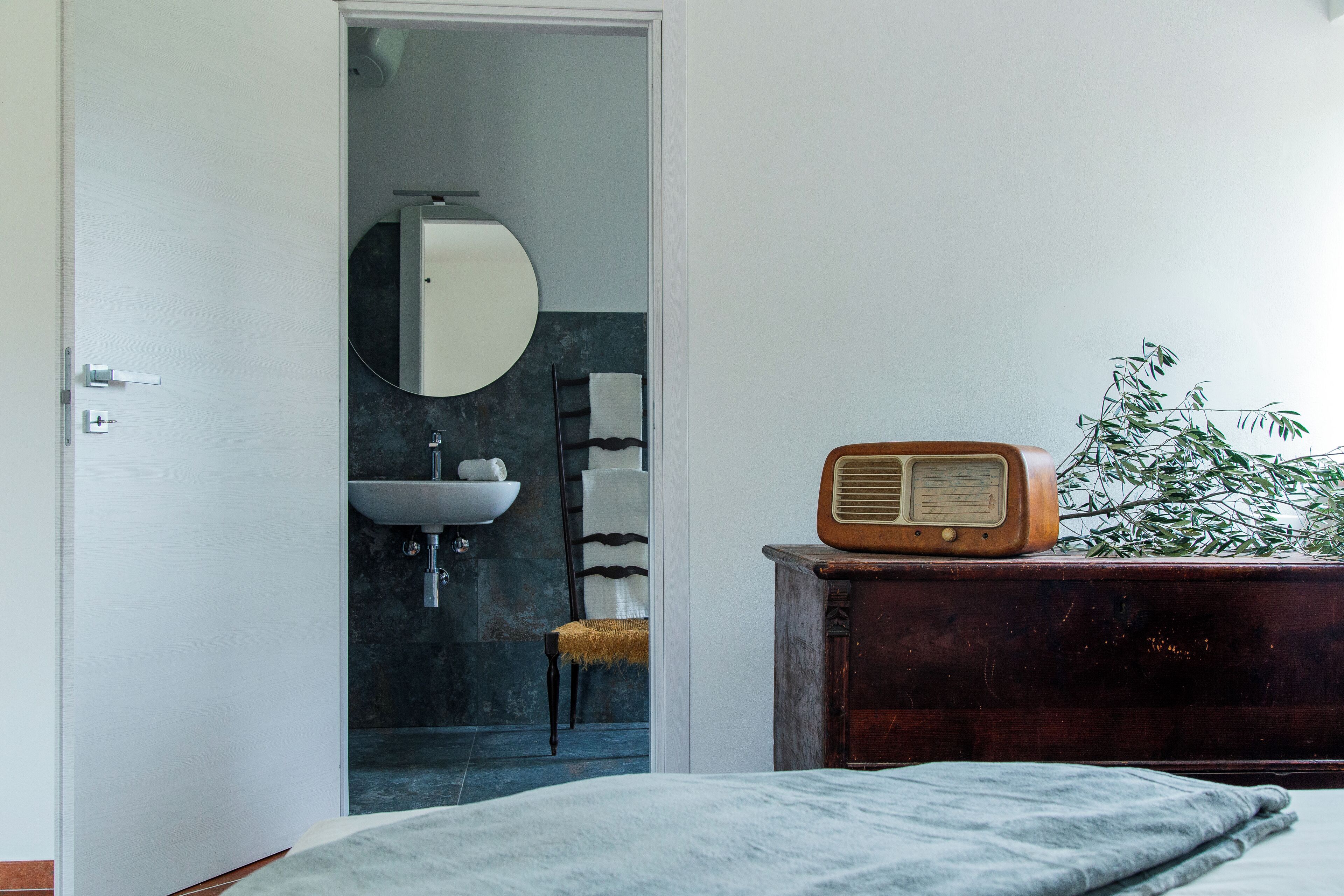 Un dormitorio con cama, cómoda, radio, planta y baño visible a través de una puerta abierta.