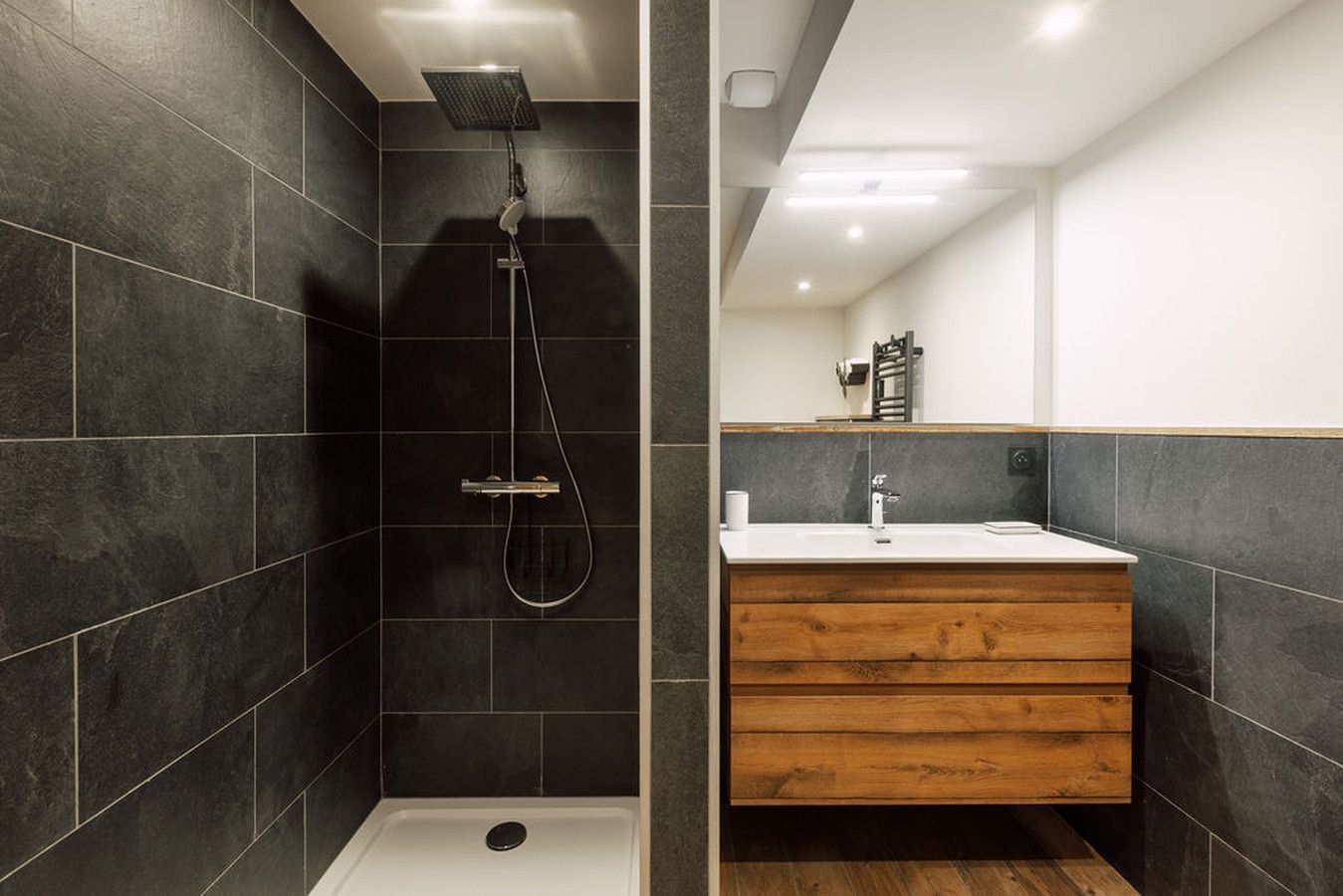 A modern bathroom with a shower, a wooden vanity, and a mirror.