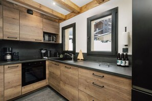 A modern kitchen with wooden cabinets, a black countertop, and a window with a view of a building. - Le Gypaète, Prodains, Morzine (Morzine)