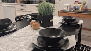 Une cuisine moderne avec des meubles blancs, un four à micro-ondes, une machine à café et une table à manger agrémentée de bols et d’assiettes noirs.
