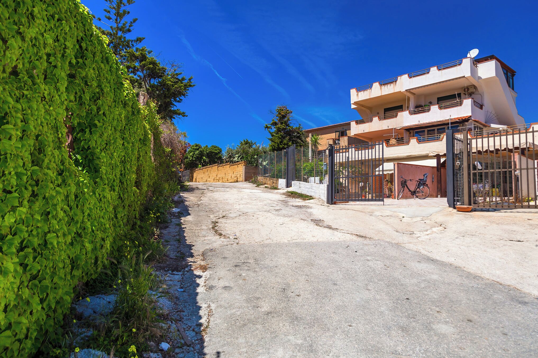A two-story building with a gated entrance, a bicycle parked outside, and a clear blue sky.