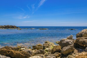 Una costa rocosa con aguas azul cristalina y una tierra a lo lejos.
