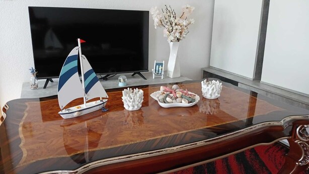 Een houten tafel met een model zeilboot, decoratieve spullen en een televisie in een kamer.