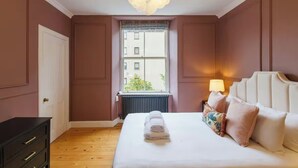 A bedroom with a large bed, a window with a view, a radiator, and a nightstand with a lamp. - Cosy & Stylish Edinburgh City Flat - Pass the Keys (Edinburgh)