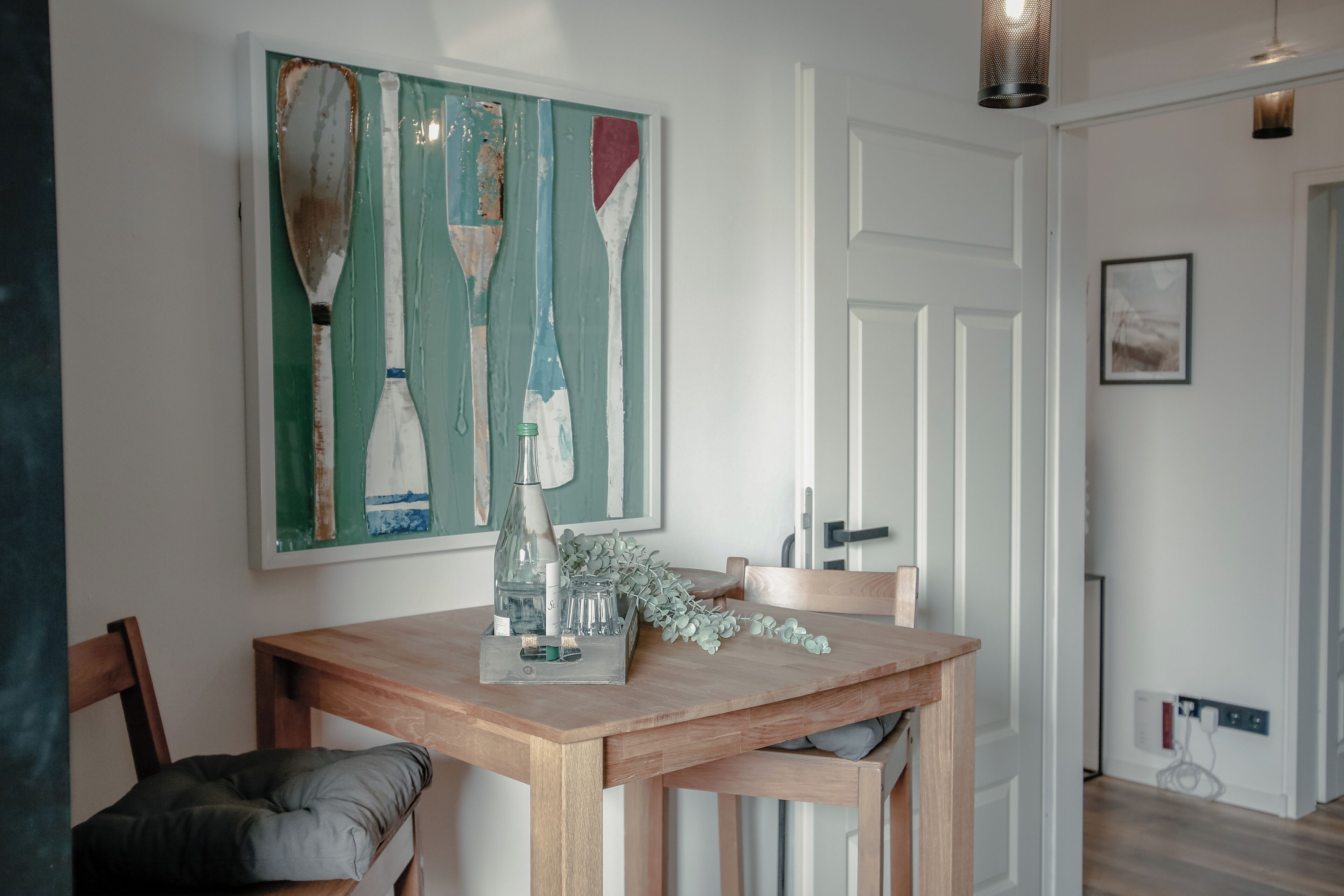 A dining area with a wooden table, chairs, and a painting of oars on the wall.