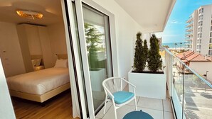 Un balcon équipé d’un lit, d’une chaise, d’une table et offrant une vue sur la mer et les bâtiments.