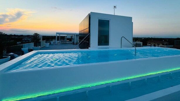 Une piscine sur le toit, au design moderne, entourée d’espaces de détente en plein air et offrant une vue dégagée sur les toits de la ville au coucher du soleil.