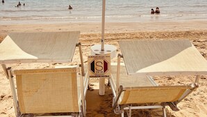 Une plage bordée d’une rangée de transats et d’un grand parasol.