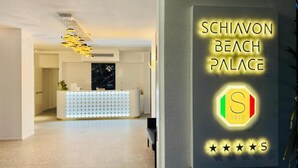 Un espace d’accueil au design moderne, un comptoir de réception et une enseigne indiquant le nom « Schiavon Beach Palace », accompagnée d’un logo et de l’année « 1919 ».