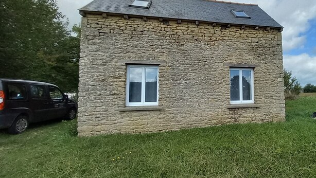 Een stenen huis met twee ramen en een schuin dak.