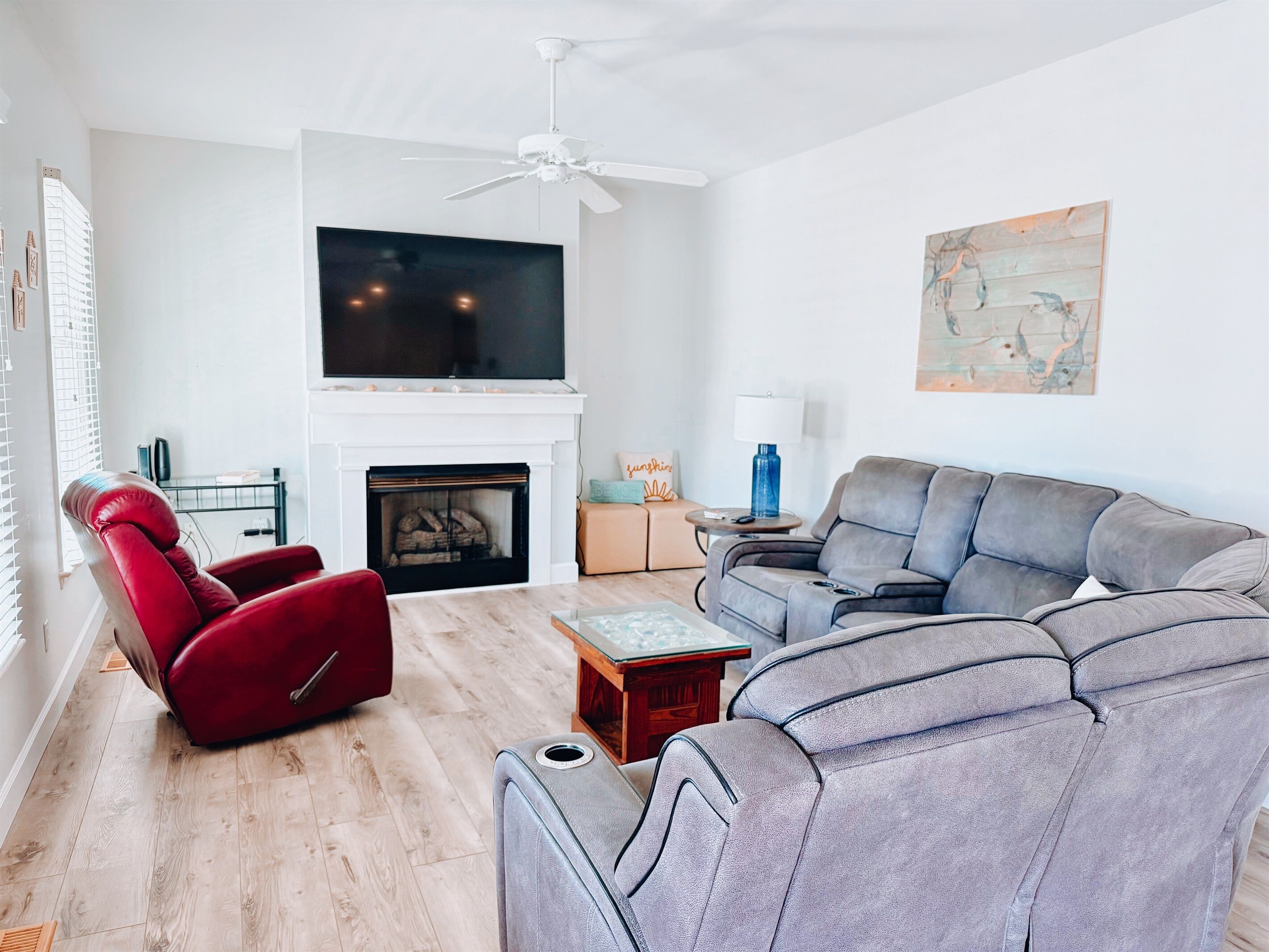 A modern living room with a fireplace, a red recliner, a grey sofa, and a ceiling fan.