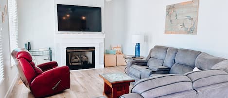 A modern living room with a fireplace, a red recliner, a grey sofa, and a ceiling fan.
