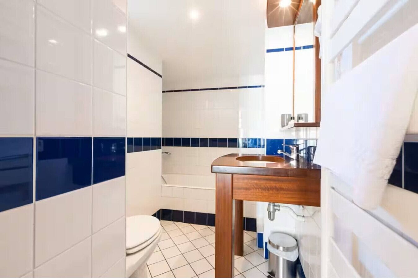 Ein Badezimmer mit weißen und blauen Fliesen, einem Holzbadezimmer-Möbel, einem Waschbecken, einer Toilette und einer Duschkabine.