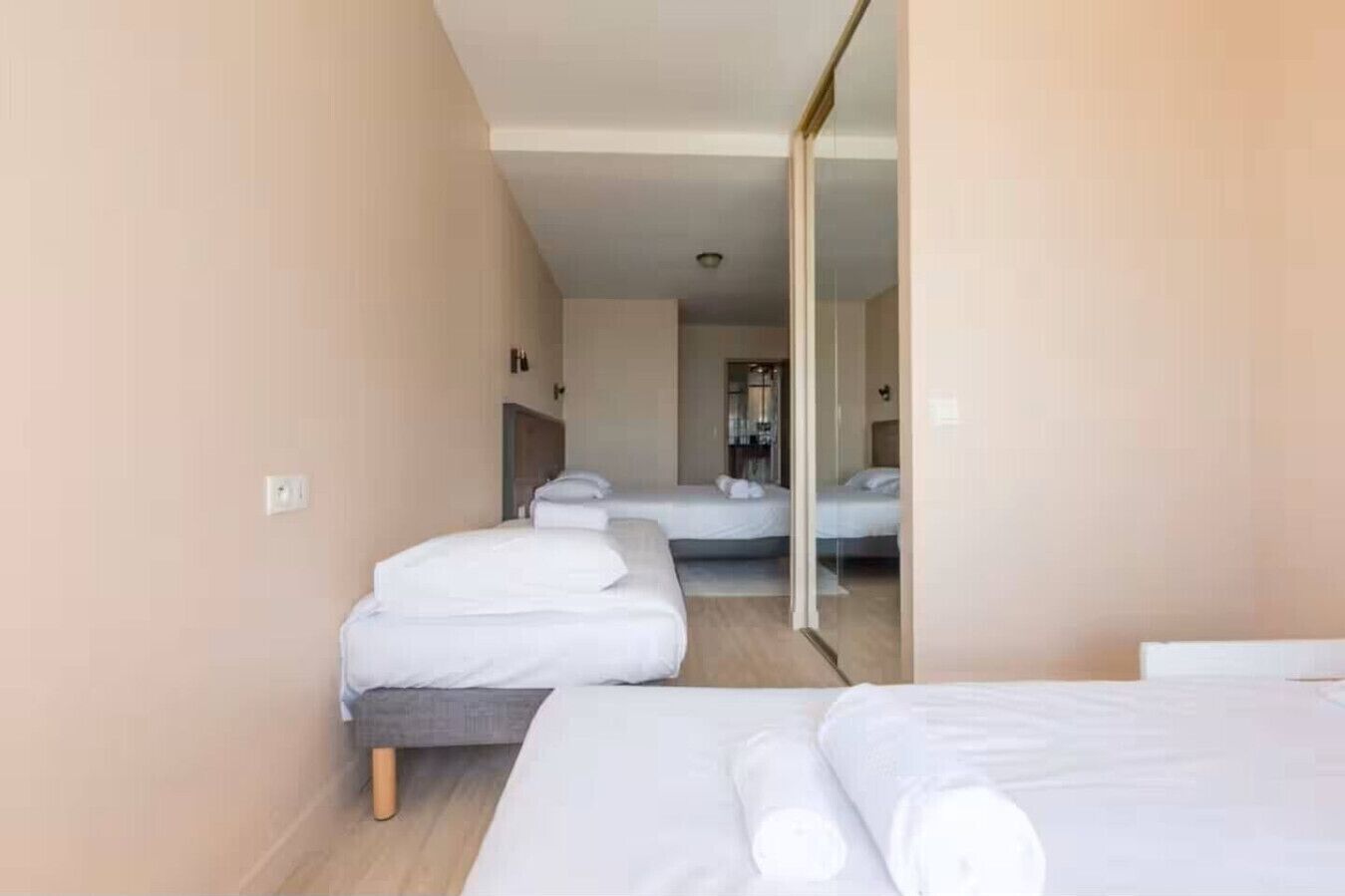 A hotel room with three beds, a mirror, and a wooden floor.