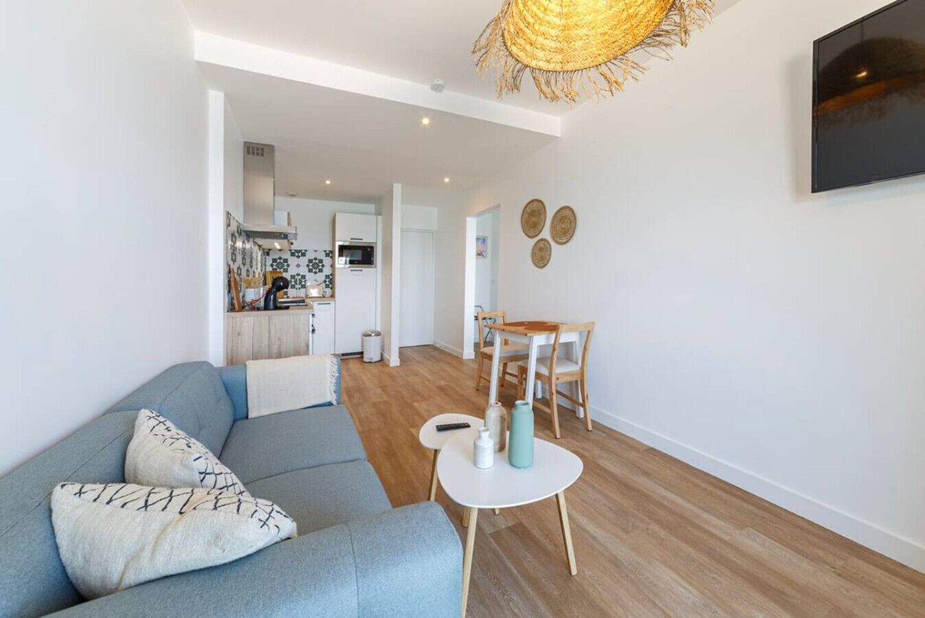 Un salon moderne comprenant un canapé, une table à manger avec des chaises, un coin cuisine et un téléviseur fixé au mur.
