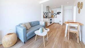 A modern living room with a sofa, a small round table, and a dining area with a wooden table and chairs.