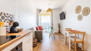 A modern kitchen with a coffee machine, a dining area with a table and chairs, and a living area with a sofa and a view of the sea. - Au pied de la plage 1 - Vue mer (Cancale)