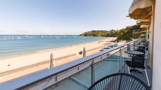 A balcony with a view of a beach, a glass railing, and outdoor furniture. - Au pied de la plage 1 - Vue mer (Cancale)